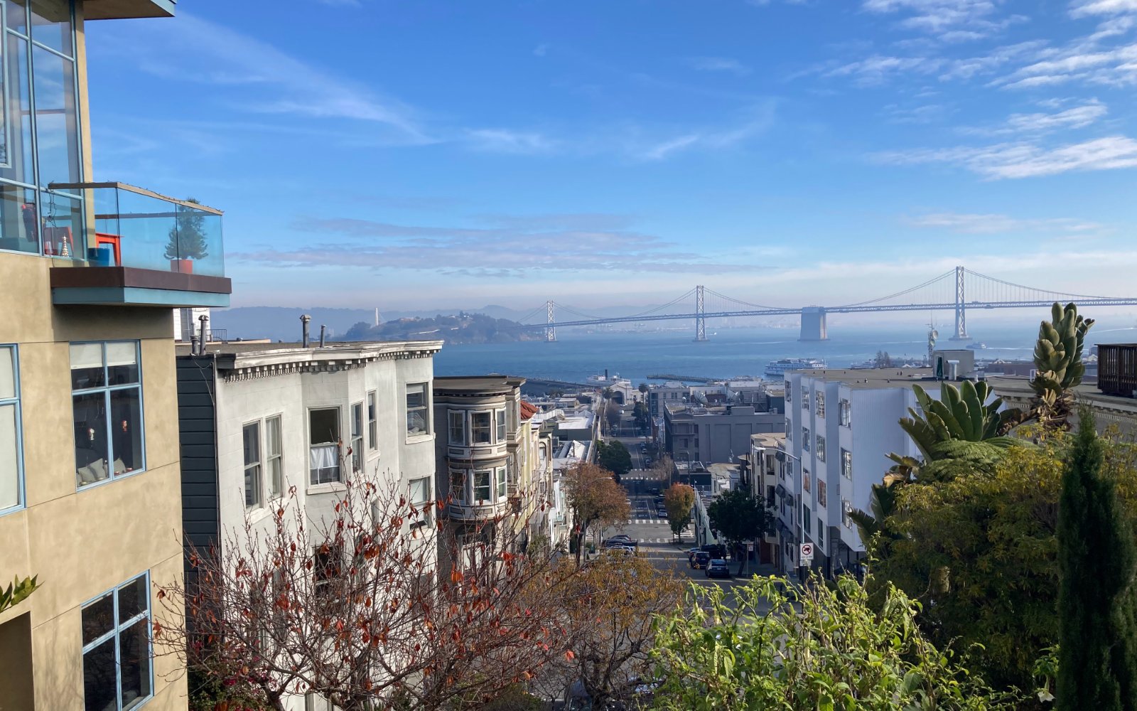 Steep San Francisco street lined with apartment buildings, looking down toward the San Francisco-Oakland Bay Bridge