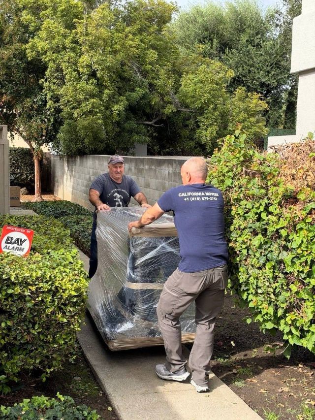 Two movers in California Movers shirts carrying a stretch-wrapped sofa